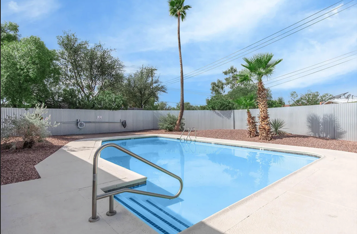 Inviting outdoor swimming pool surrounded by lush palm trees, offering a serene and private oasis under a clear blue sky.