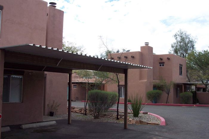 Charming adobe-style apartment complex with shaded carport and serene desert landscaping.