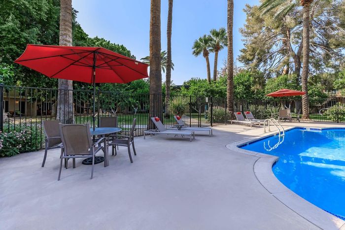 Inviting outdoor pool area with lounge chairs, red umbrellas, and lush palm trees, perfect for relaxation and entertainment.