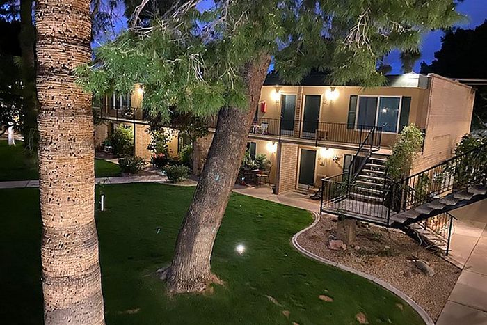 Charming apartment building with beautifully landscaped greenery, featuring outdoor lighting and inviting patios at dusk.