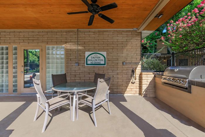 Charming patio area with a sleek glass table set, stylish ceiling fan, and modern outdoor grill, ideal for entertaining and relaxation.