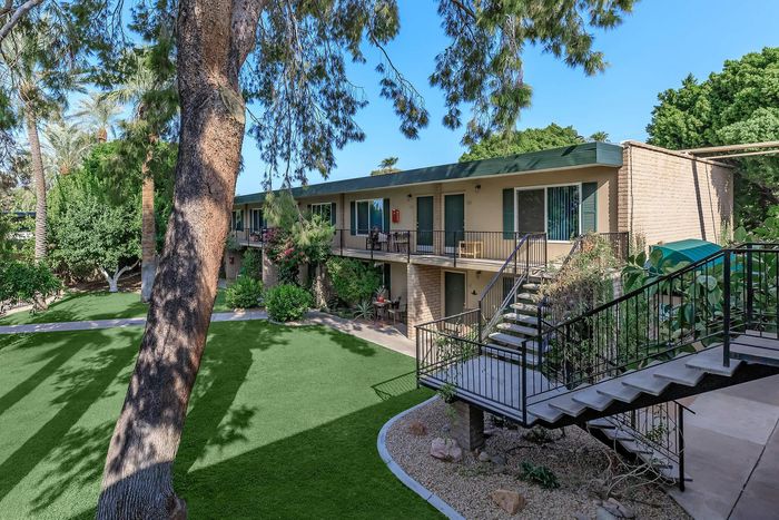 Charming two-story apartment complex surrounded by lush greenery and mature trees, featuring modern balconies and inviting outdoor spaces.