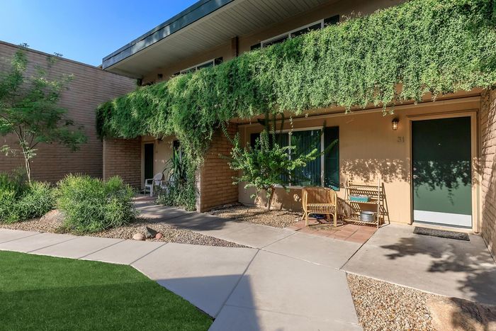 Charming apartment entrance with lush greenery, cozy seating area, and inviting pathway.