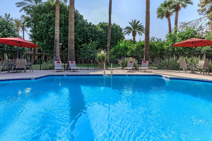 Stunning resort-style pool surrounded by lush greenery and palm trees, with inviting lounge chairs and vibrant red umbrellas.