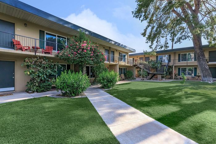 Charming apartment complex with lush greenery, vibrant flowers, and inviting balconies set against a clear sky.