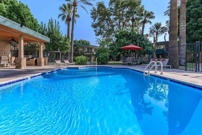 Inviting outdoor pool area with sparkling blue water, surrounded by lush greenery and palm trees, complete with shaded seating and lounge chairs for relaxation.