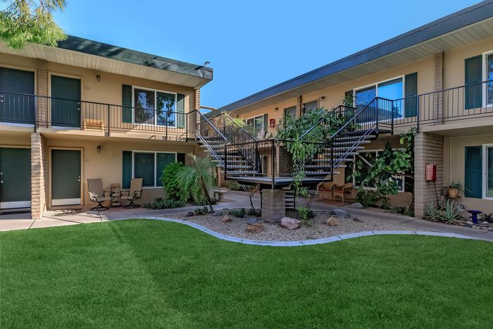 Charming courtyard view of a modern apartment complex with lush greenery, stylish outdoor seating, and vibrant landscaping.