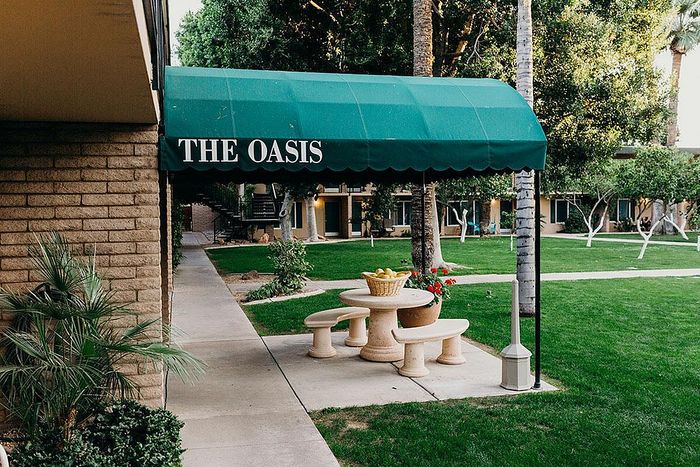 Charming courtyard at The Oasis featuring lush greenery, a cozy seating area with stone benches, and vibrant flowers, offering a serene escape.