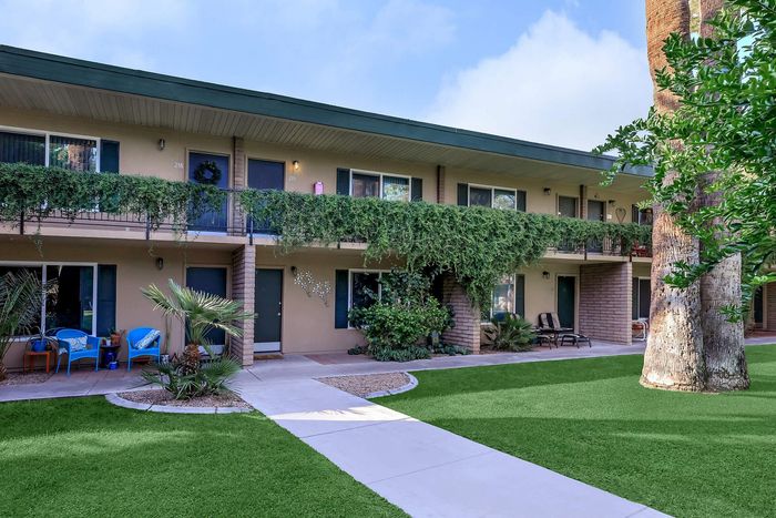 Charming two-story apartment complex with lush greenery and cozy outdoor seating areas.