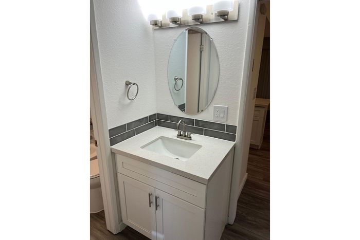 Modern bathroom vanity with sleek white cabinet, quartz countertop, oval mirror, and stylish light fixtures complementing contemporary decor.