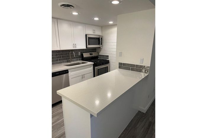 Modern kitchen featuring sleek white cabinetry, stainless steel appliances, and a stylish quartz countertop with ambient recessed lighting.