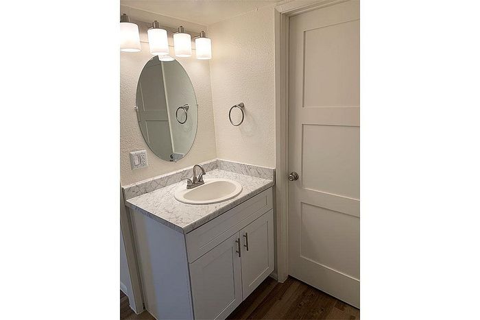 Elegant bathroom with a chic marble countertop, stylish oval mirror, and modern lighting.