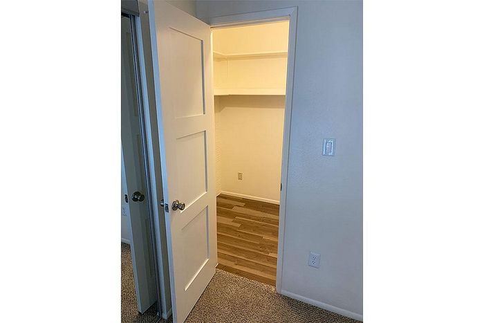Inviting walk-in closet with wooden flooring and white shelving, perfect for ample storage.
