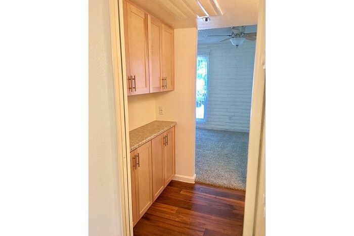 Inviting hallway with polished wood floors, ample storage cabinets, and a cozy living space adorned with natural light.