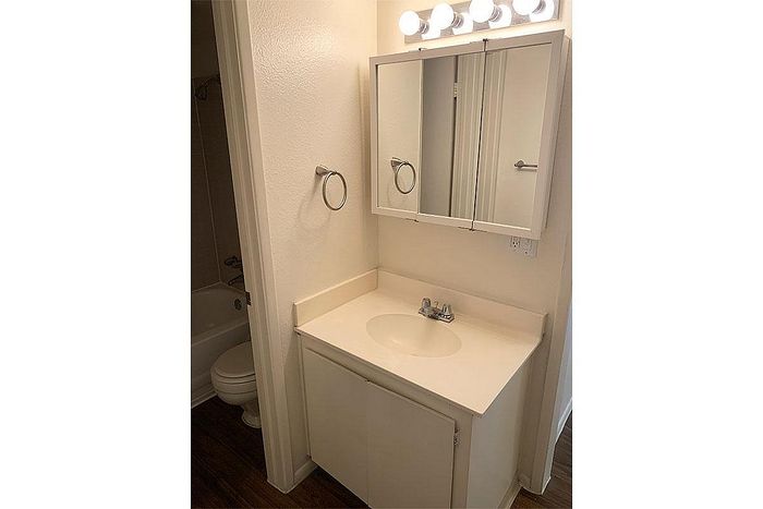 Bright bathroom featuring a sleek vanity with mirror, modern lighting, and a cozy bathtub in the background.