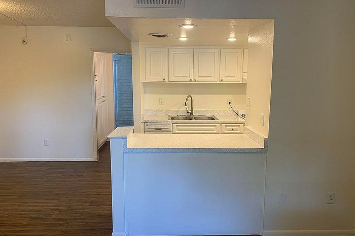 Charming open kitchen with white cabinetry and modern lighting, featuring a sleek countertop and hardwood floors.