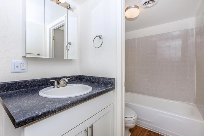 Modern bathroom featuring a sleek black countertop with a built-in sink, elegant white cabinetry, and a tiled bathtub area with ambient lighting.