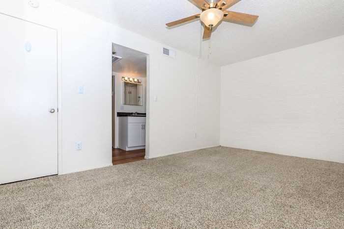 Bright, spacious apartment room with plush carpeting, ceiling fan, and elegant bathroom view, perfect for modern living.