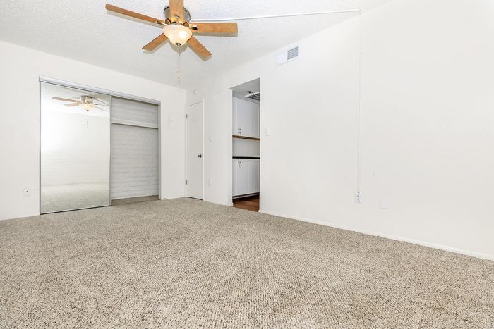 Spacious room with plush carpet, a stylish ceiling fan, mirrored closet doors, and bright neutral walls.