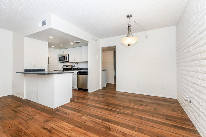 Modern apartment with elegant hardwood floors, featuring a sleek kitchen with stainless steel appliances and a stylish light fixture.