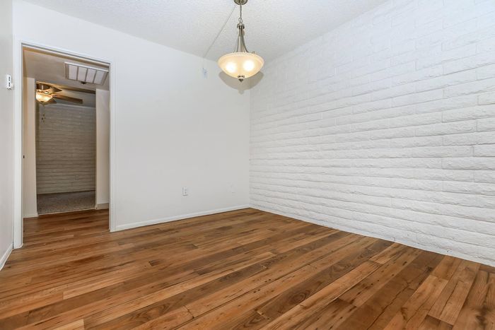 Inviting room with warm wooden flooring, white brick accent wall, and elegant ceiling light.