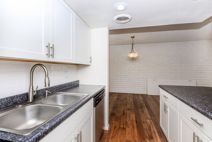 Modern kitchen with sleek white cabinets, elegant double sink, and stylish countertops leading to an open dining area with a charming light fixture.