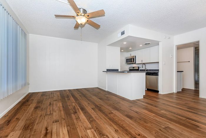 Bright and modern open-concept living area with sleek hardwood floors, contemporary ceiling fan, and a stylish kitchen equipped with stainless steel appliances.