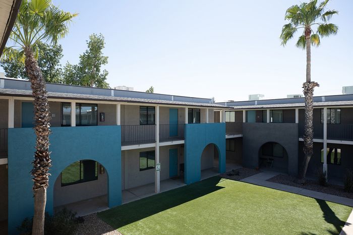 Charming two-story apartment building with vibrant blue accents, surrounded by lush palm trees and a manicured lawn.