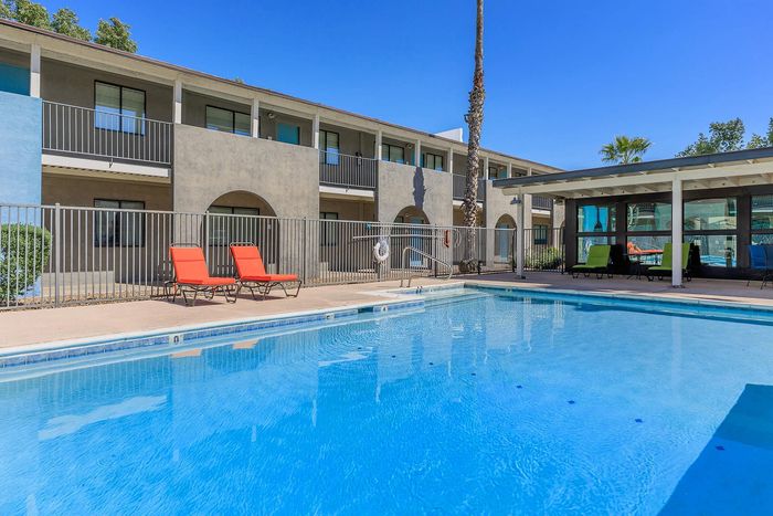 Inviting apartment complex featuring a sparkling blue swimming pool with cozy red lounge chairs, perfect for relaxation and enjoyment.