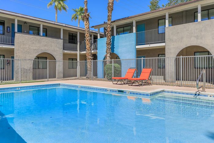 Vibrant apartment complex with inviting swimming pool, sun loungers, and tropical palm trees in a sunny courtyard.
