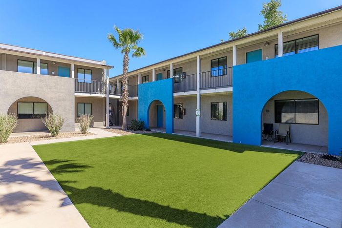 Charming apartment complex with a vibrant blue facade, surrounded by lush greenery and inviting pathways.