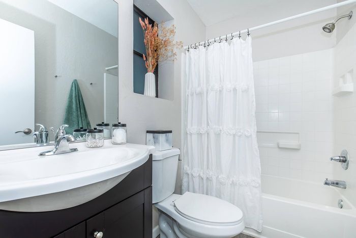 Inviting bathroom featuring a modern vanity with chrome fixtures, a pristine white bathtub with a decorative shower curtain, and elegant floral accents for a touch of sophistication.