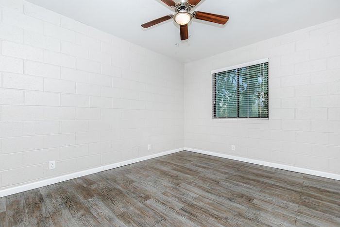 Bright and spacious room with modern wooden flooring and a ceiling fan, featuring a large window with tranquil outdoor views.