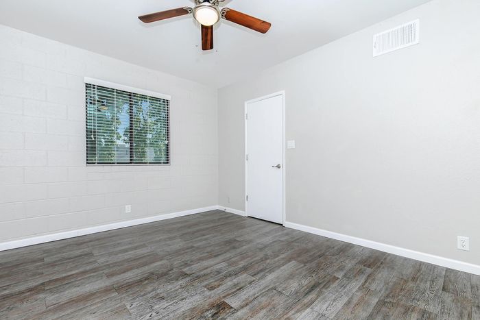 Bright, modern room with elegant wood flooring, ceiling fan, and large window offering natural light.