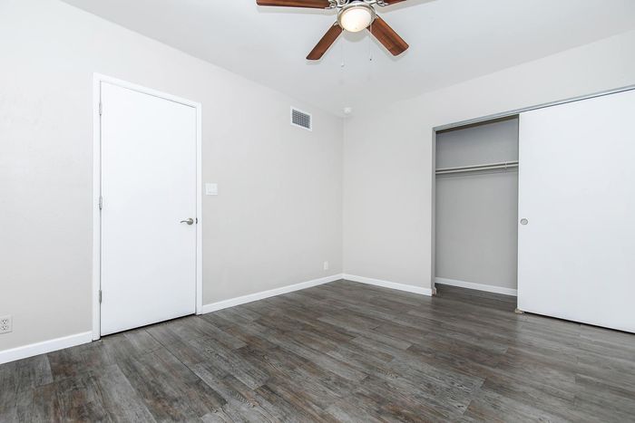 Bright and airy bedroom featuring sleek wood flooring, a spacious closet, and a modern ceiling fan.