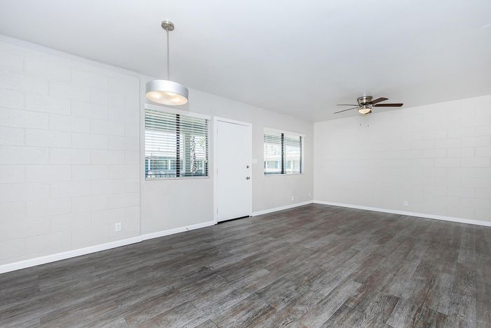 Modern living area with elegant wood flooring, bright windows, and stylish ceiling fan, offering potential for a personalized touch.