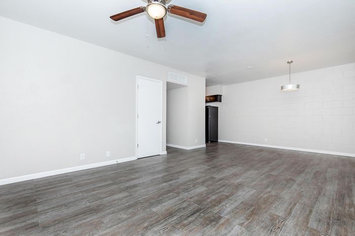 Modern apartment with sleek hardwood flooring, ceiling fan, and elegant lighting, offering ample open space in a bright living area.