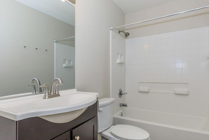 Bright and modern bathroom featuring a sleek vanity with stylish fixtures, a pristine bathtub with classic tile surround, and a large mirror.