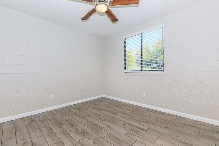 Bright and spacious room with sleek tiled flooring, a ceiling fan, and large window offering natural light.