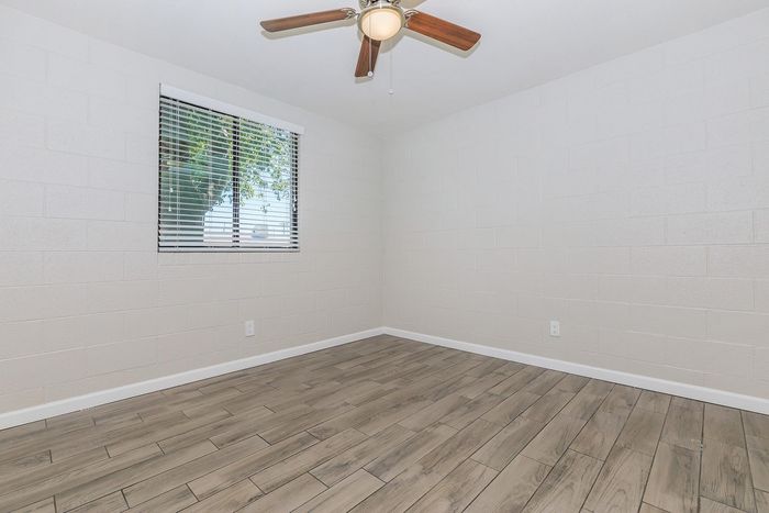 Bright and airy unfurnished room with elegant wood flooring, a ceiling fan, and a large window offering natural light.