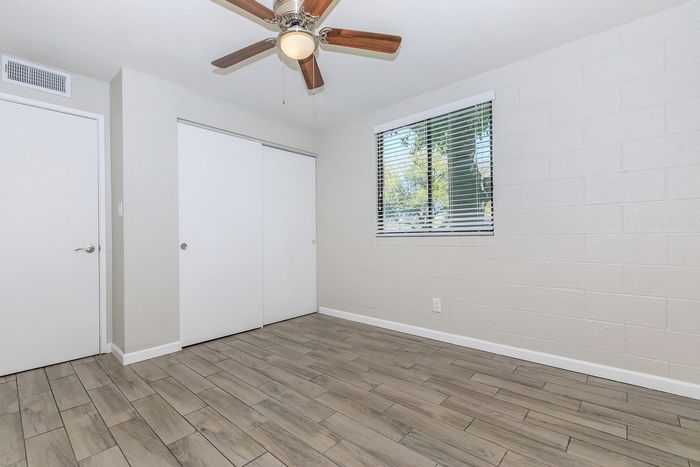Bright and airy bedroom with sleek hardwood floors, a ceiling fan, and a large window offering natural light.