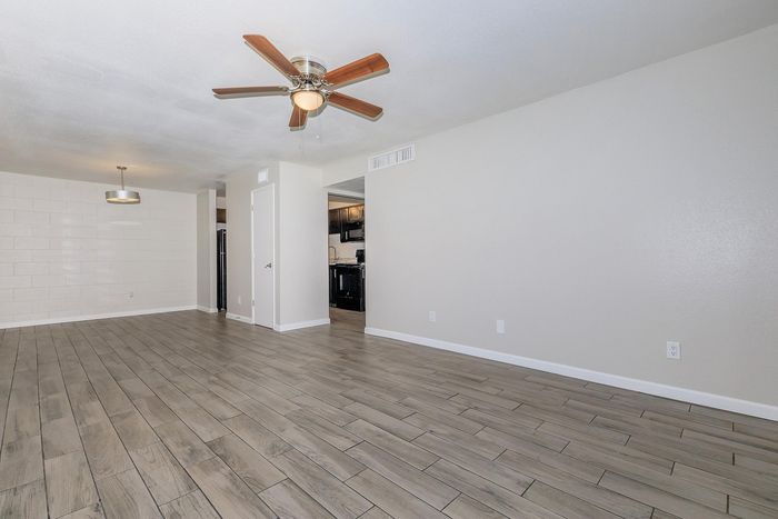 Bright and spacious living room with elegant wood flooring, modern ceiling fan, and open access to kitchen area, ideal for entertaining.