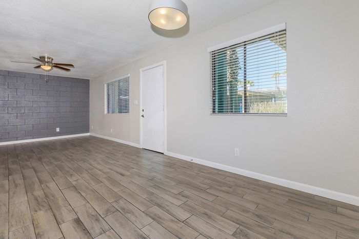 Bright and airy living room with stylish wood flooring, modern ceiling fan, and large windows offering abundant natural light.