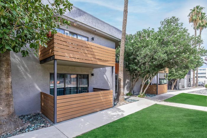 Charming apartment exterior featuring stylish wooden balconies, lush greenery, and a well-maintained lawn.
