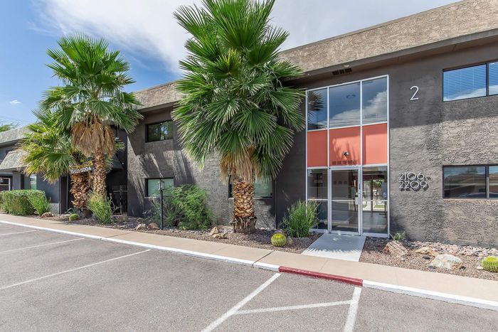 Modern apartment complex entrance with lush palm trees and a stylish facade, offering a welcoming ambiance.
