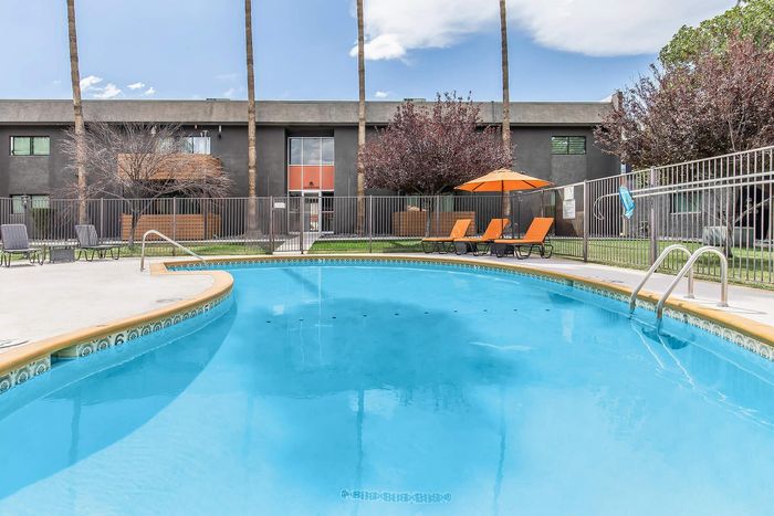 Inviting outdoor pool with lounging area and vibrant orange umbrellas, set amidst a modern apartment complex surrounded by lush trees.