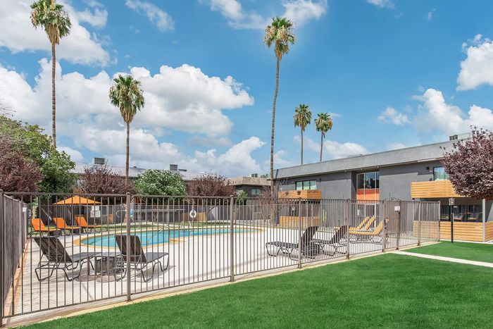 Inviting apartment complex with a sparkling swimming pool surrounded by palm trees and modern outdoor seating.