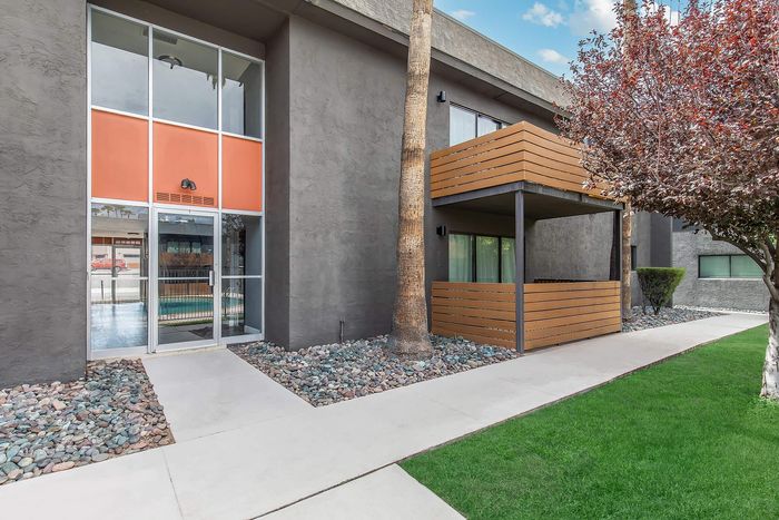 Modern apartment exterior with a sleek gray facade, wooden balcony, lush green lawn, and inviting entrance.