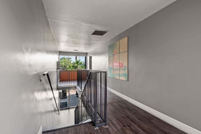 Bright, modern hallway with sleek wood flooring, large windows offering lush outdoor views, and a vibrant flamingo artwork, enhancing the welcoming ambiance.