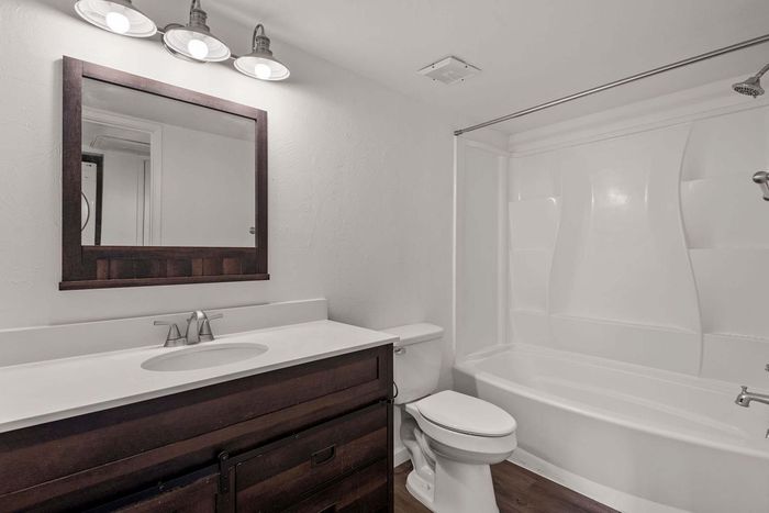 Charming bathroom with rustic vanity, sleek countertop, and modern lighting over a spacious bathtub.